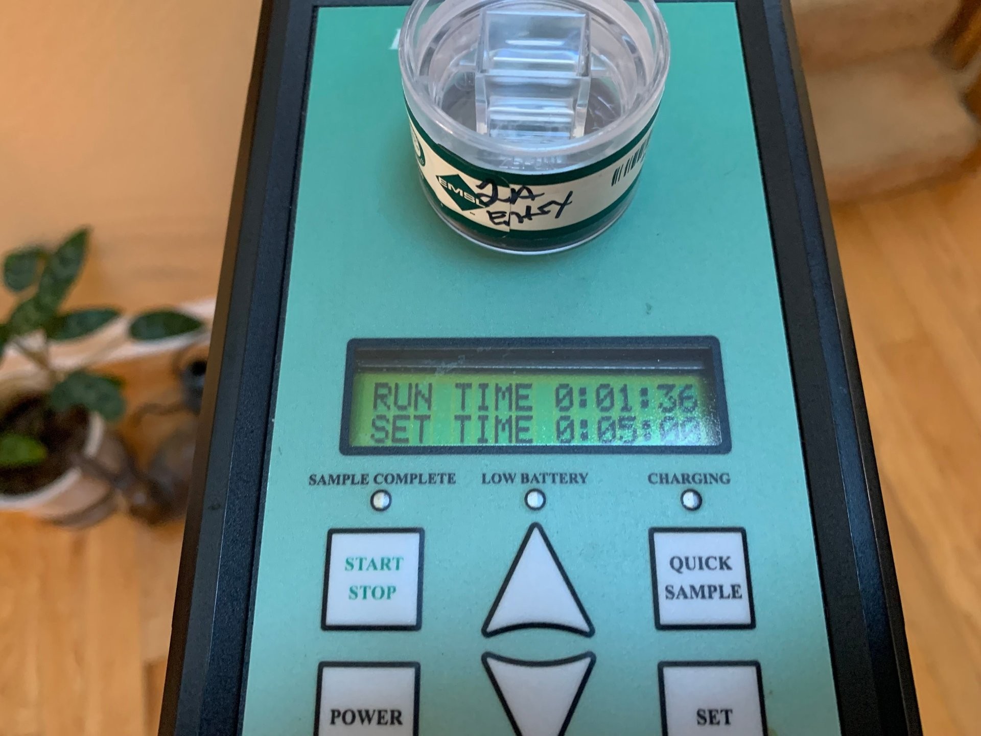 Digital scale with turquoise display showing run time and set time, featuring buttons for power, start/stop, and quick sample functions