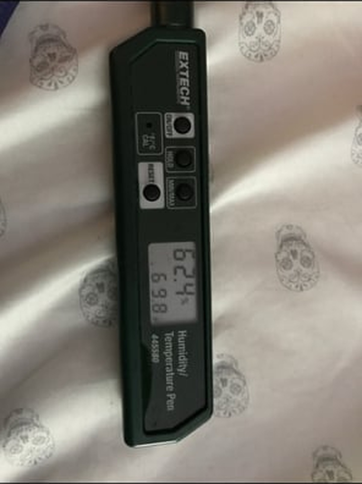 Black digital thermometer with LCD display showing temperature reading and control buttons on patterned surface